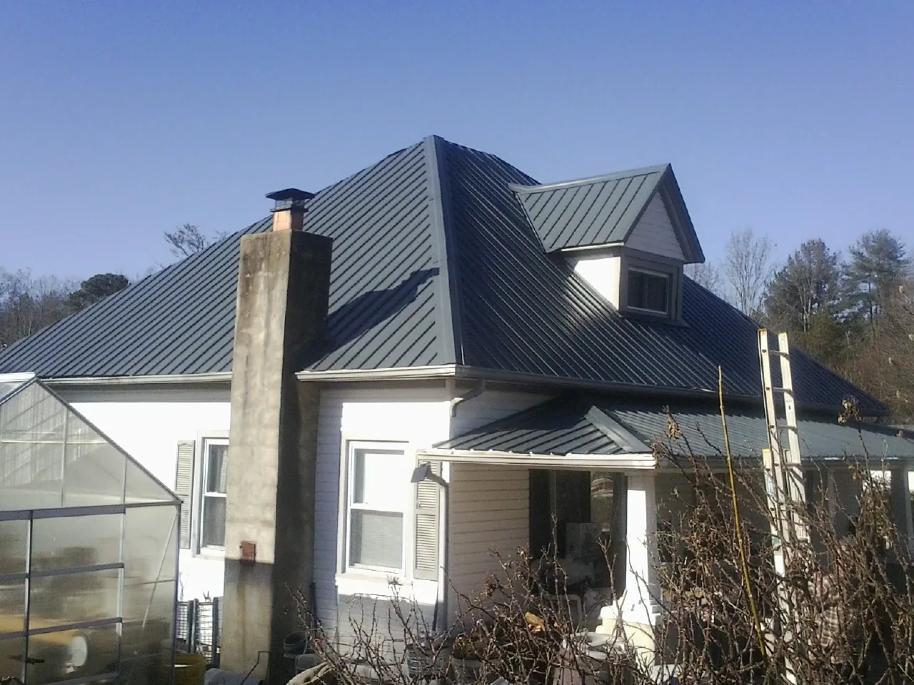 Dark blue standing seam metal roof on a white farmhouse with dormer — Slate & Tile Roof Repair by Roofing Brothers in Wayzata