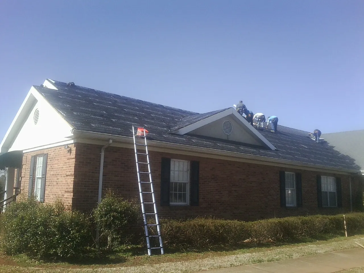 Crew tearing shingles off a brick ranch roof with a ladder set — Emergency Roof Repair work by our crew in Wayzata