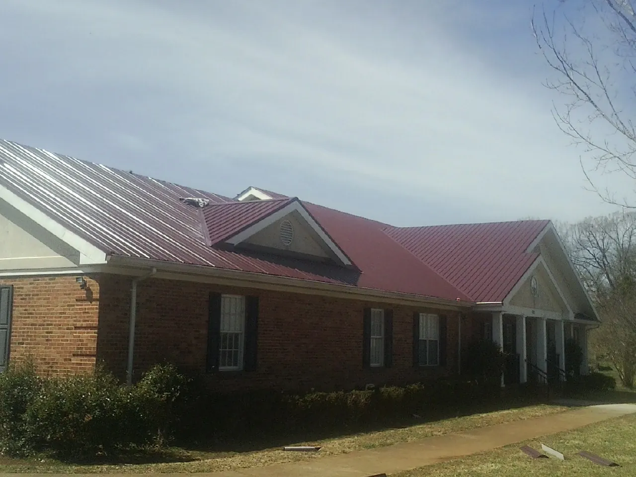 Red metal roof with gabled entries on a long brick building, from a Hail Damage Roof Repair job in Wayzata