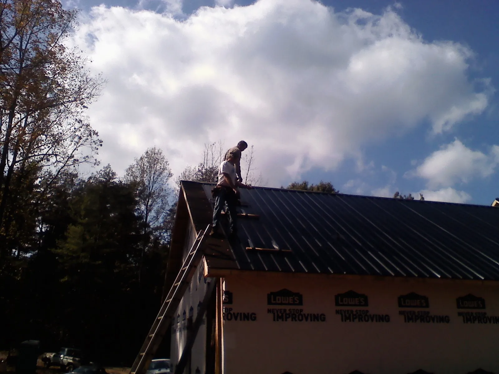 Roofer fastening dark metal panels high against a cloudy sky, from a Roof Inspection job in Wayzata
