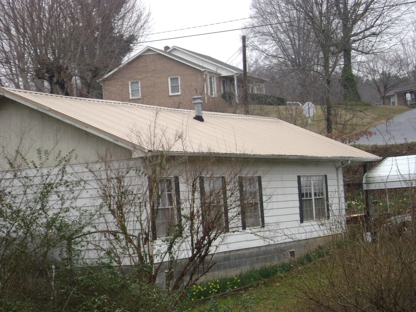 Tan metal roof on a white sided house set into a hillside — Commercial Roofing by Roofing Brothers in Wayzata
